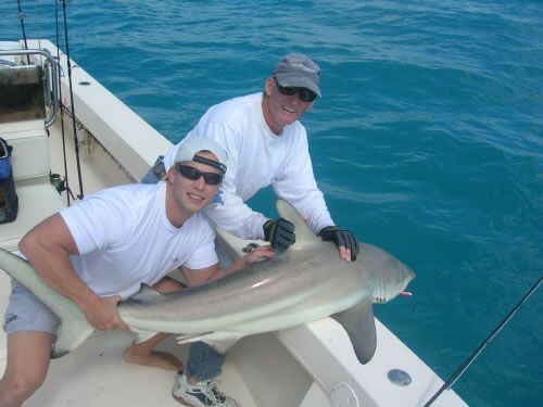 Two men on a boat holding a large shark