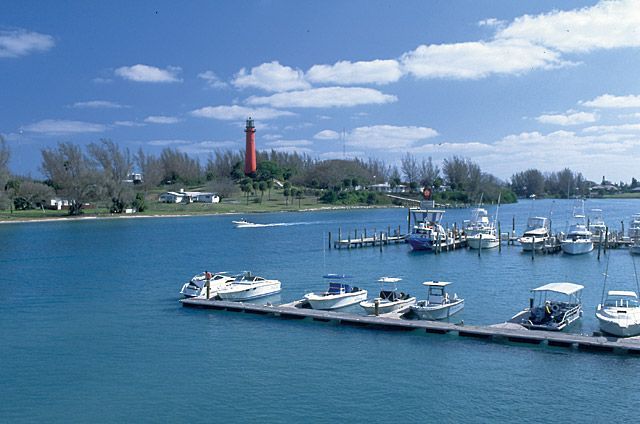 Boats are docked at a marina with a lighthouse in the background