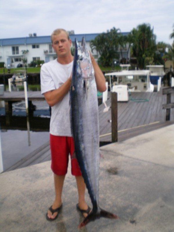 A man in red shorts is holding a large fish