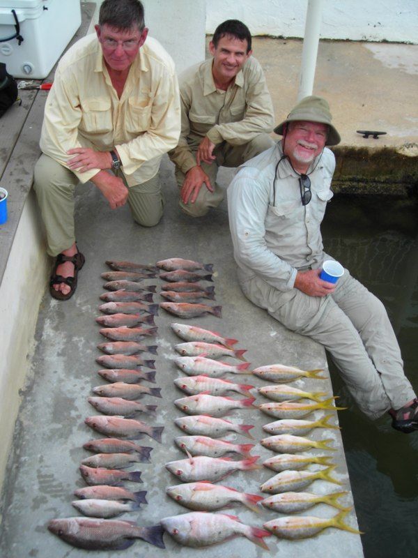 Three men are kneeling next to a pile of fish