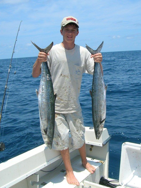 A man on a boat is holding two fish in his hands