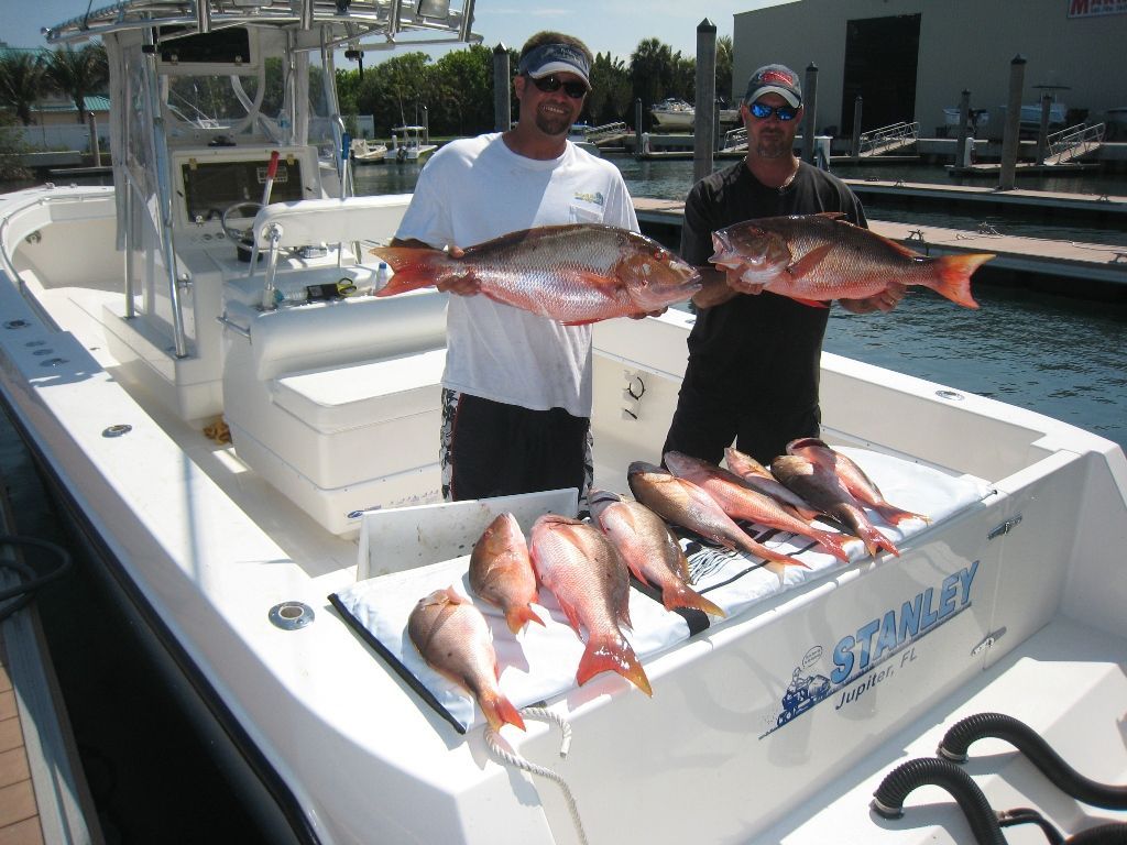 Two men standing on a boat holding a bunch of fish