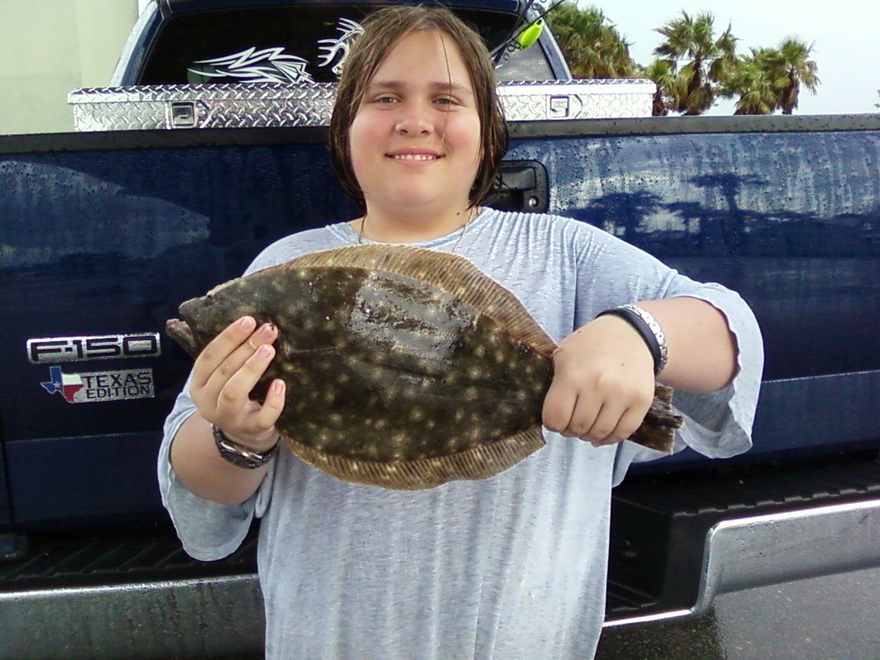 A girl holding a fish in front of a ford truck