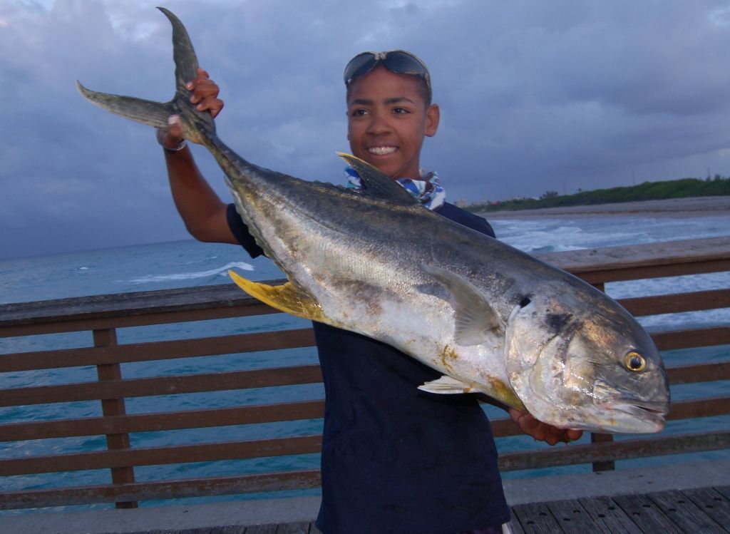 A young man is holding a large fish on a pier