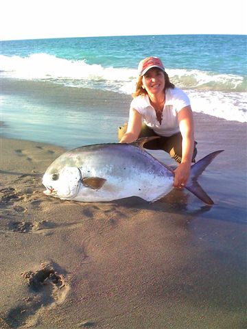 A woman is posing with a large fish on the beach