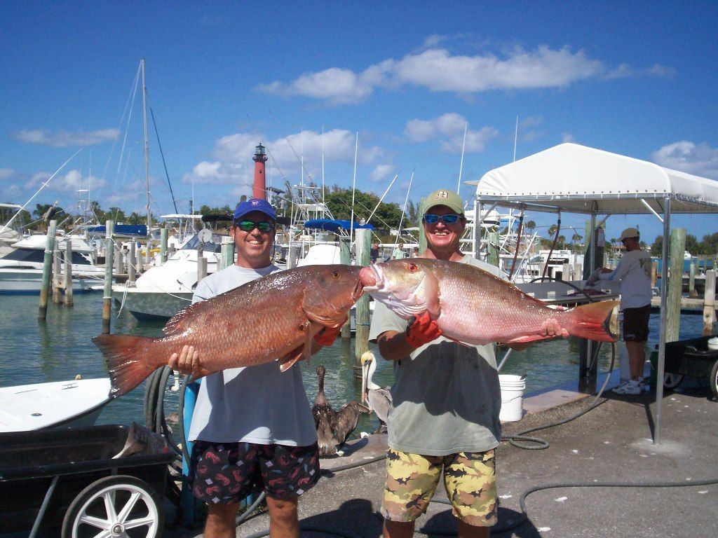 Two men holding large fish in front of a boat