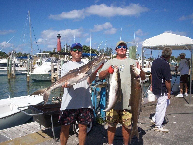 Two men holding large fish in front of boats