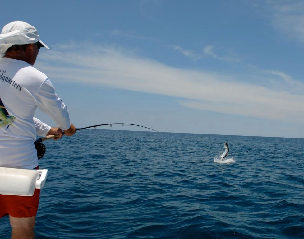 A man in a white shirt with the word fishing on it is fishing in the ocean