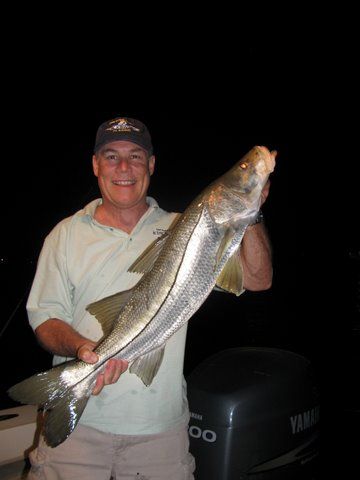A man is holding a large fish in front of a yamaha engine.
