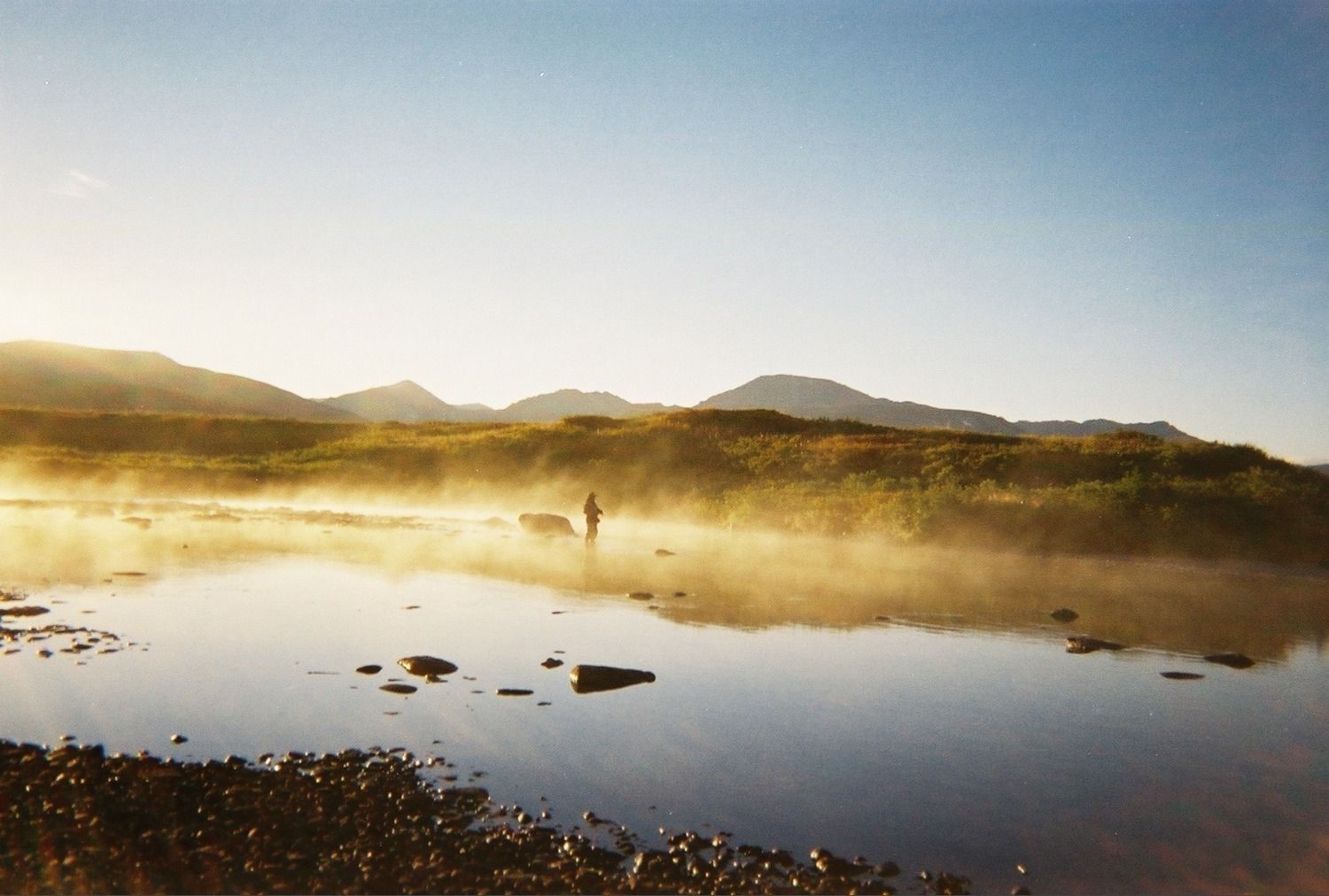 A person fishing in a foggy lake with mountains in the background
