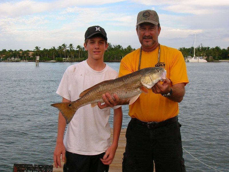 A man in a yellow shirt holds a large fish next to a boy