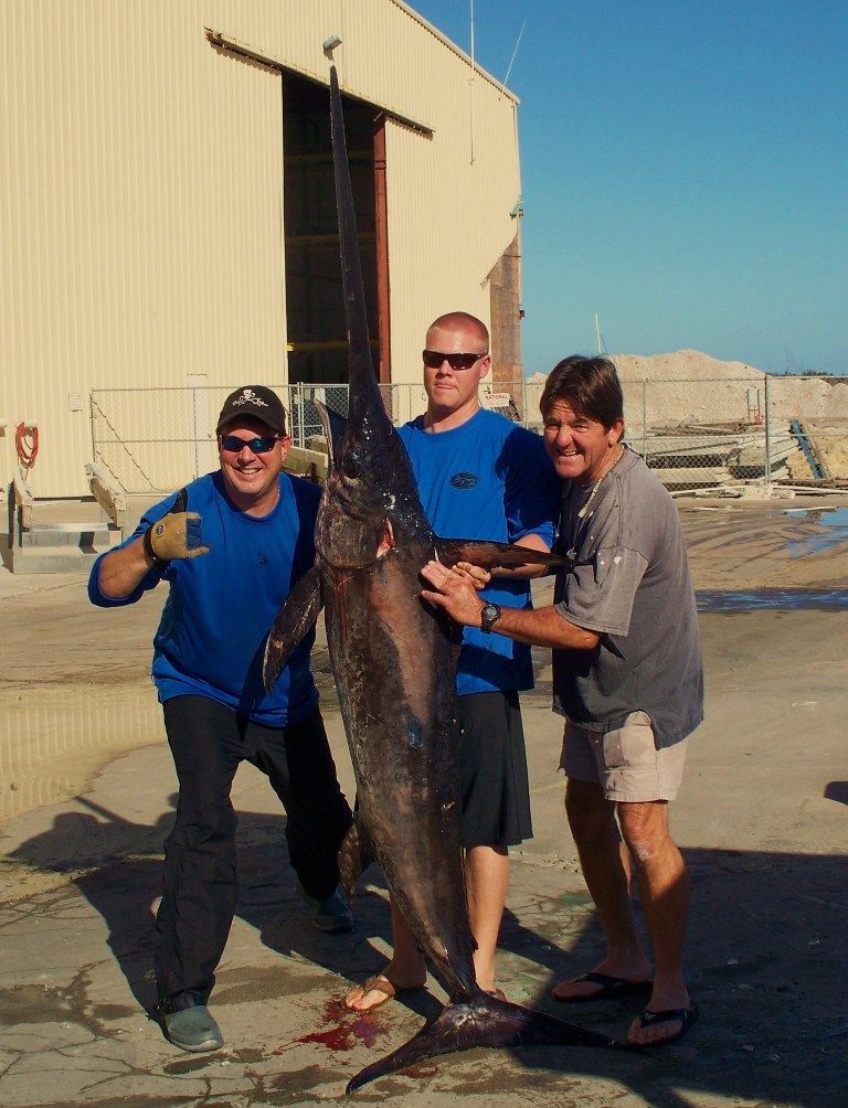 Three men holding a large fish in front of a building