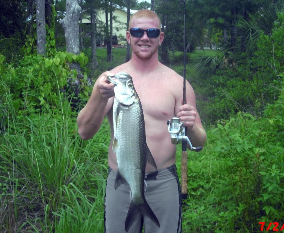 A shirtless man is holding a large fish and a fishing rod