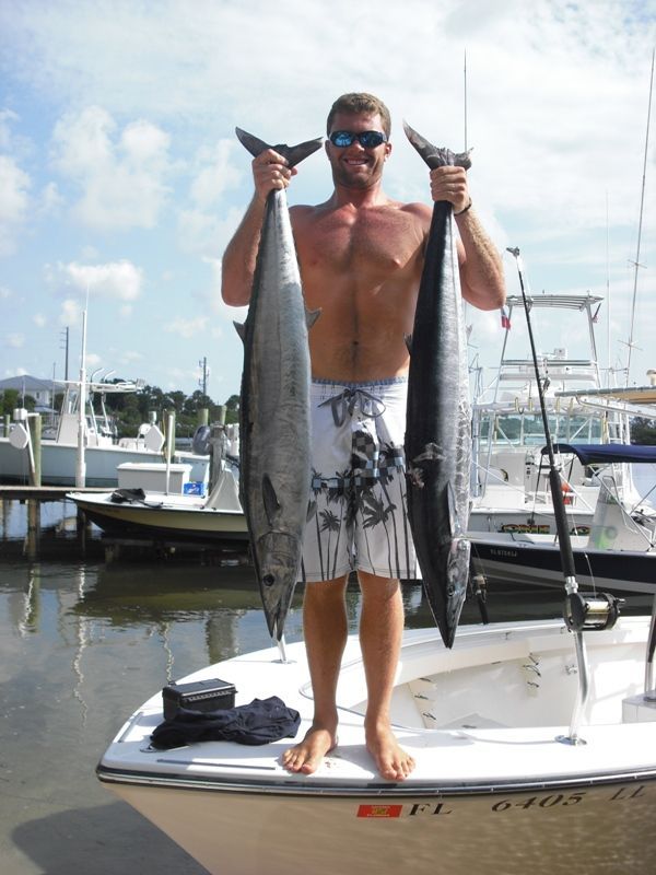 A shirtless man is standing on a boat holding two fish