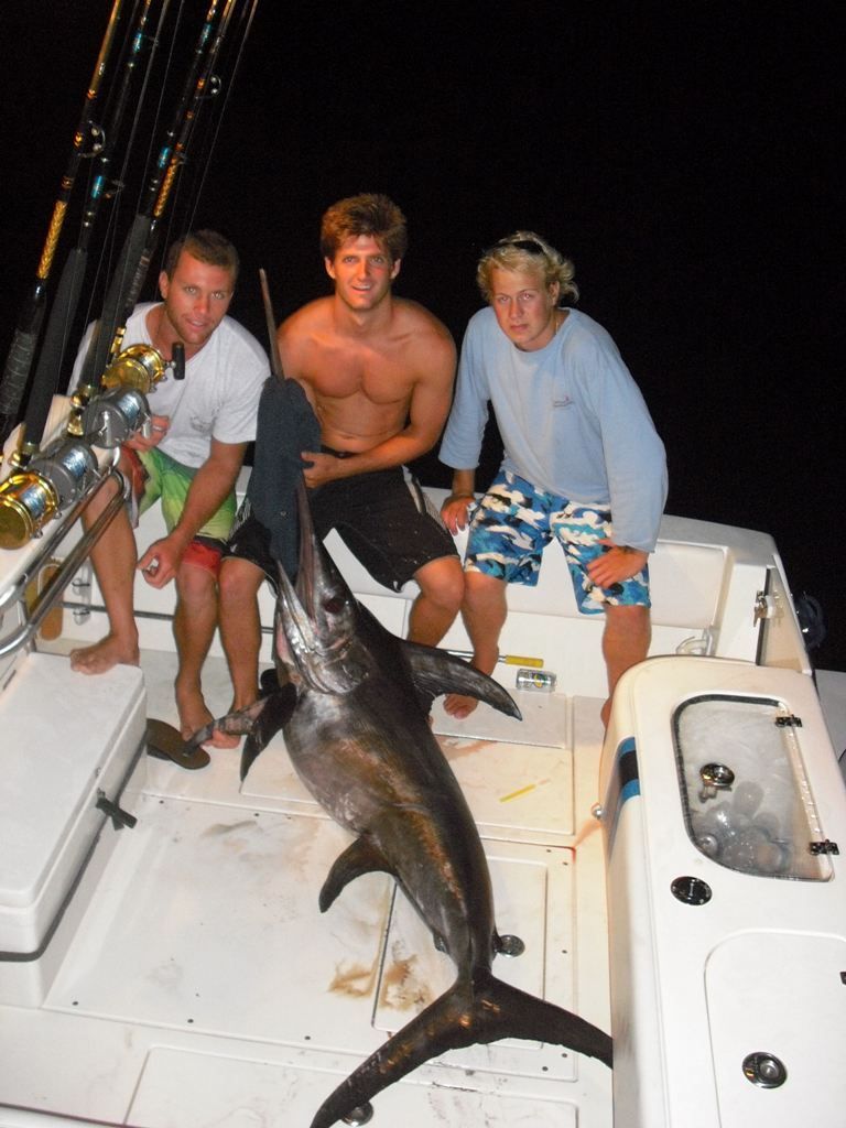 Three men sitting on a boat holding a large fish