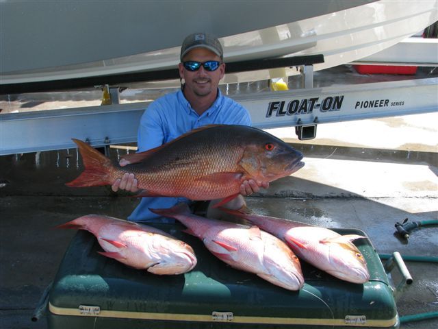 A man holding a large fish in front of a boat that says float-on