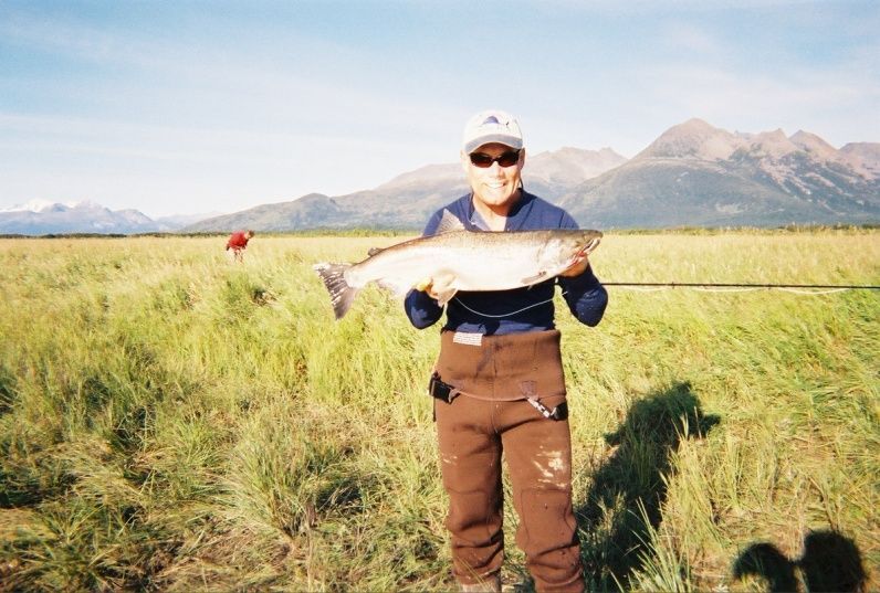 A man holding a large fish in a field with mountains in the background