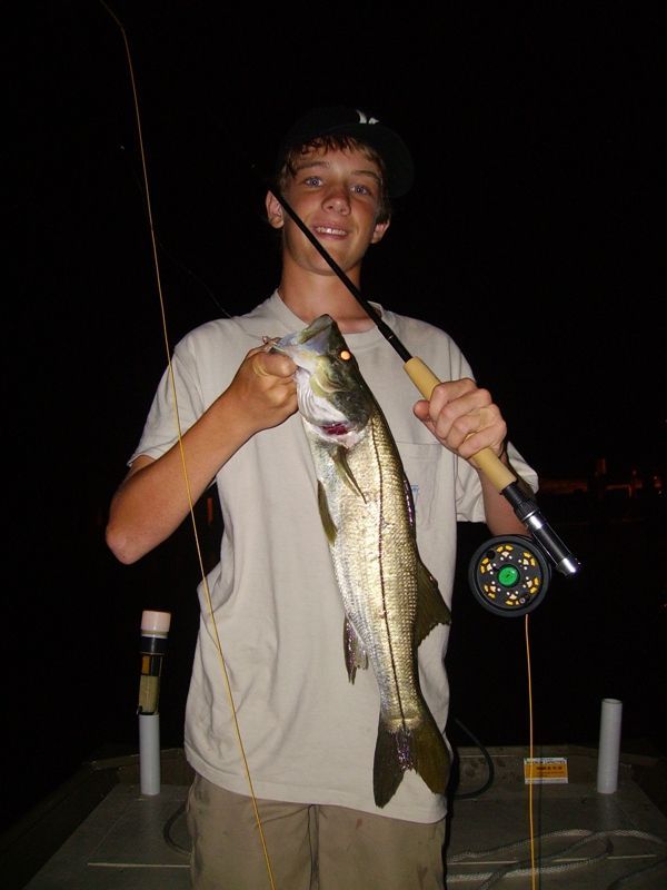 A young boy is holding a large fish and a fishing rod