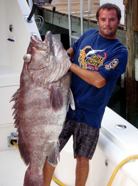 A man holding a large fish wearing a shirt that says super monkey
