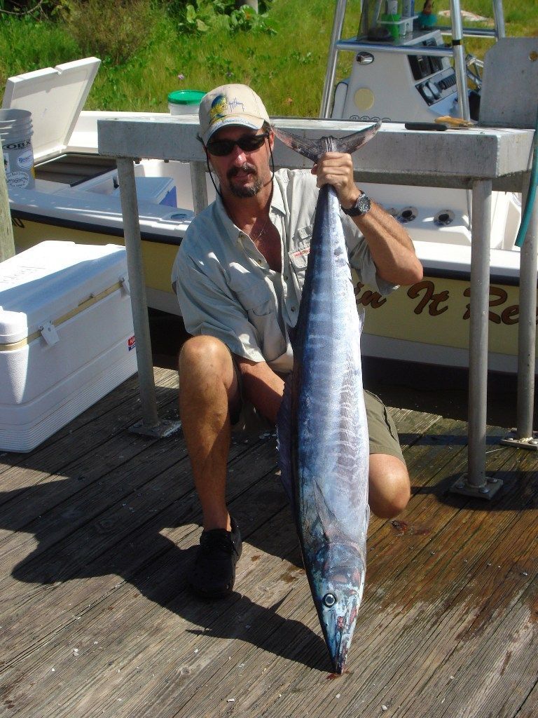 A man is kneeling down holding a large fish in front of a boat