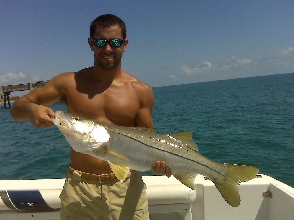 A shirtless man is holding a large fish on a boat