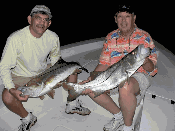 Two men sitting on a boat holding large fish