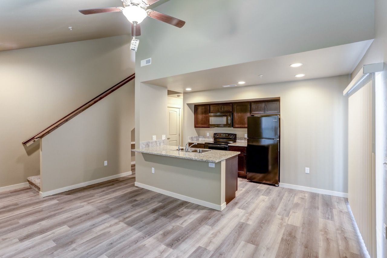 Open-concept kitchen with island, granite countertops, dark wood cabinets, and a stainless steel refrigerator.
