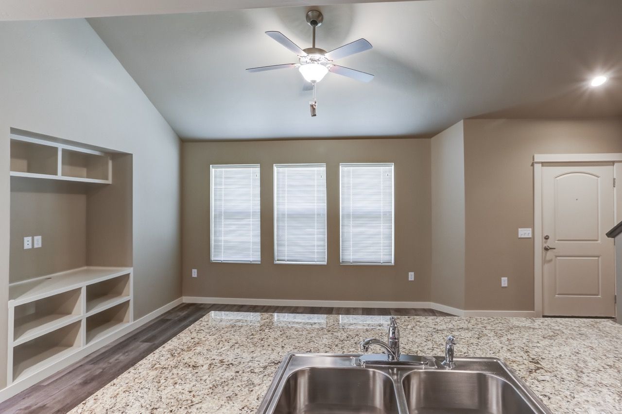 Open-concept kitchen and living area with granite island, double sink, and built-in shelves.