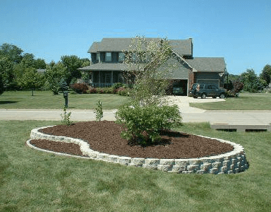Suburban house with a landscaped front yard, curved mulch bed, and small shrub near the driveway.