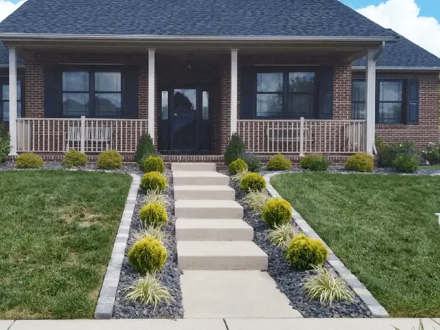 Front view of a house with a porch, central steps, and landscaped walkway and flower beds