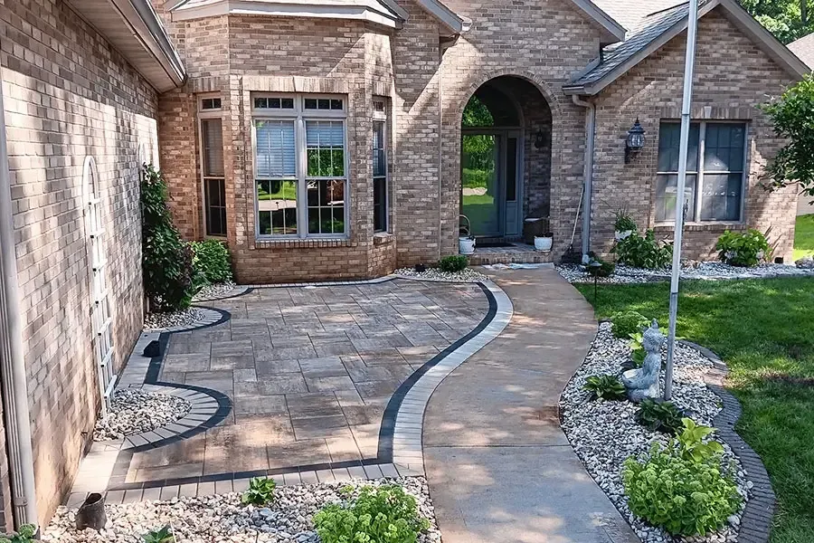 Stone front entry with curved paver walkway, landscaped beds, and arched doorway.