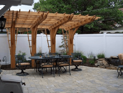 Backyard patio with a wooden pergola, outdoor dining table, potted plants, and stone paving