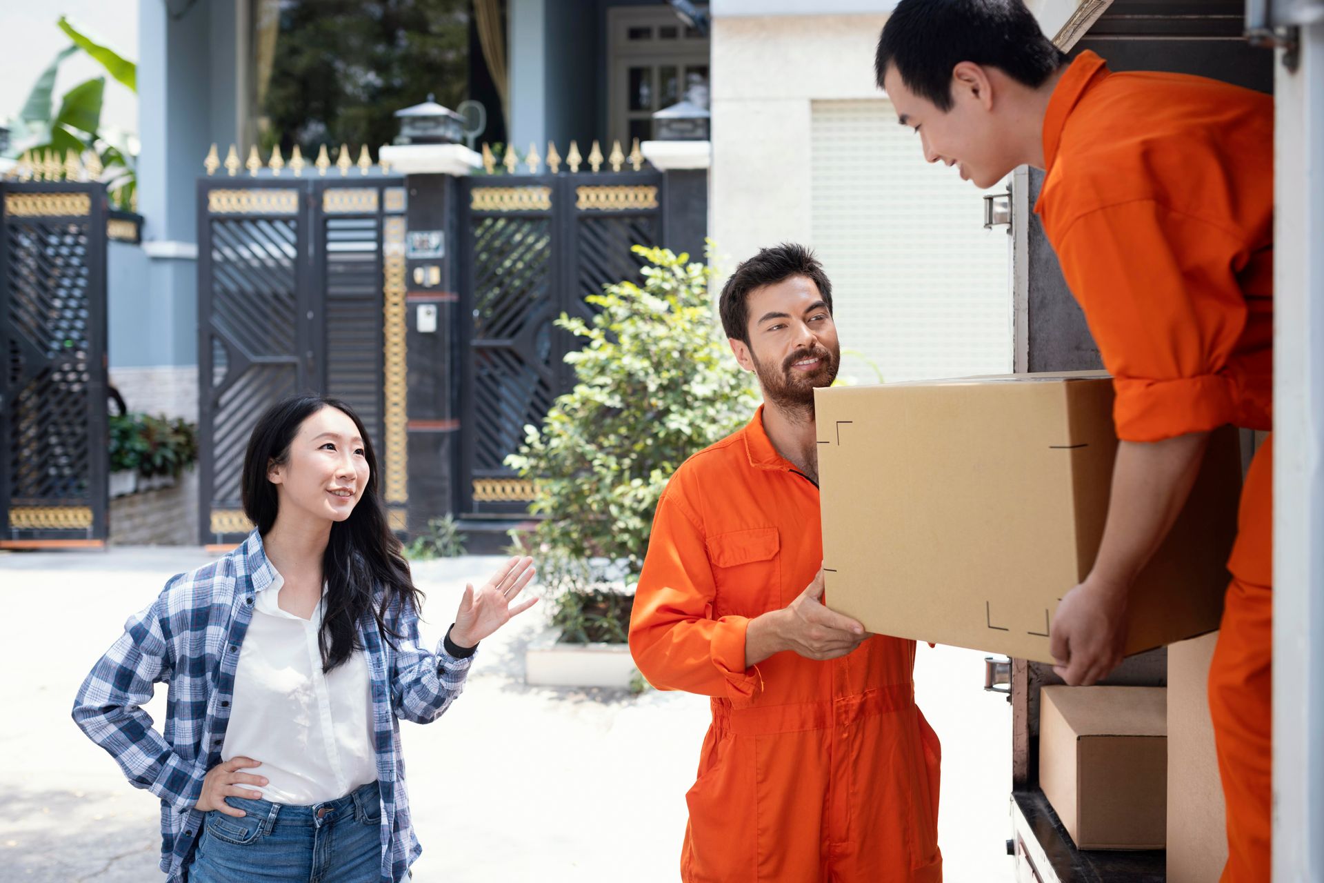 Woman watching movers unload boxes from a truck in front of a house.