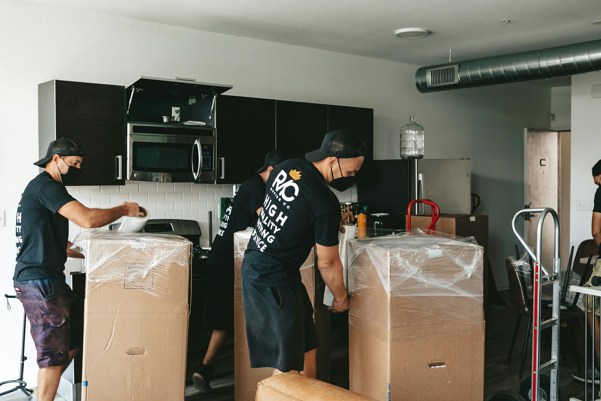 Three men moving appliances in boxes with wraps.