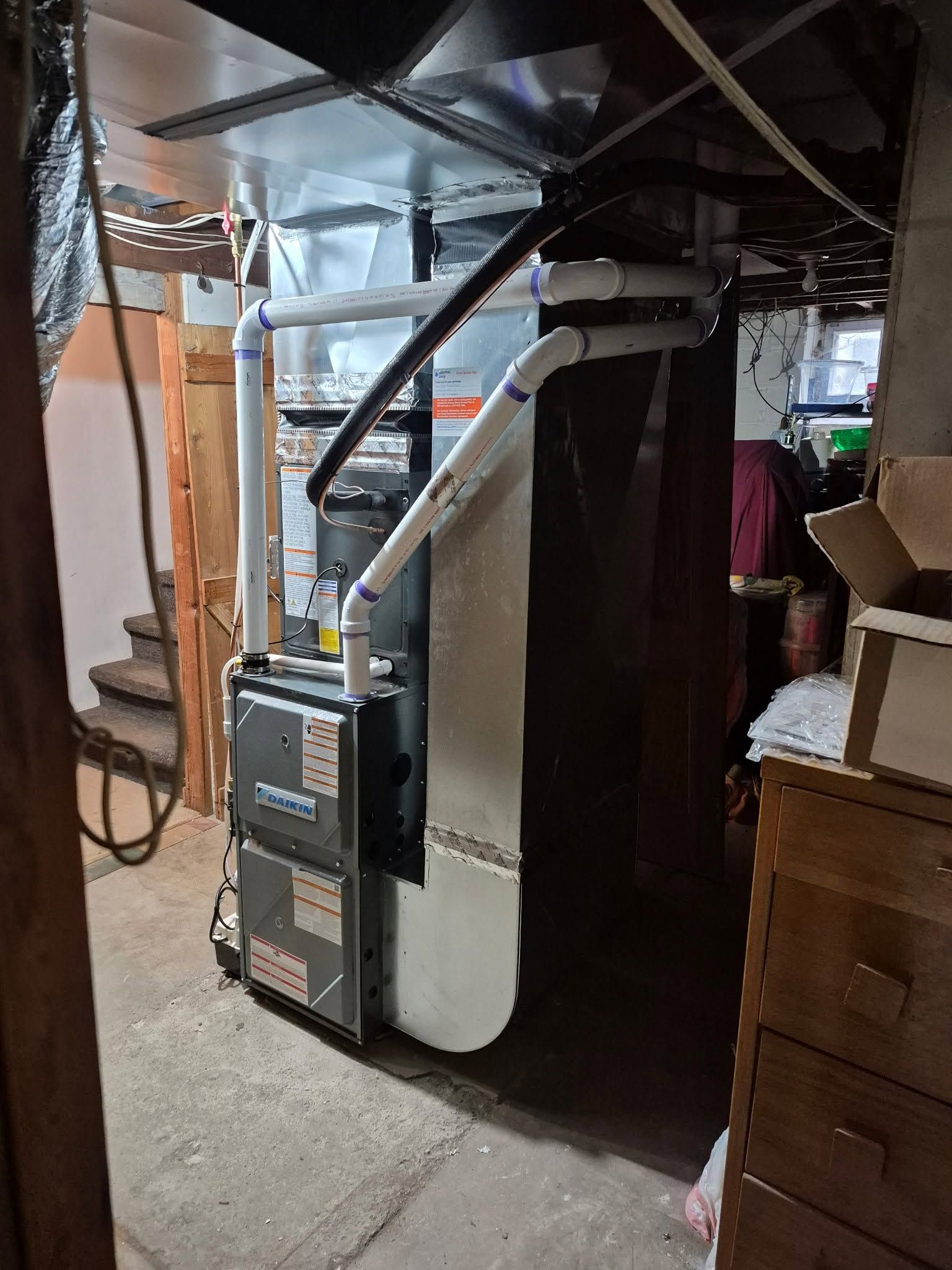 Furnace and HVAC ductwork in a basement utility area beside storage furniture.