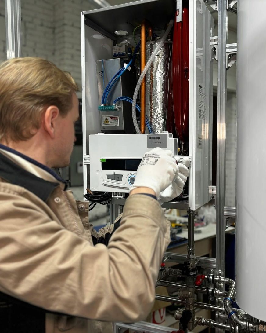 Technician adjusting a control panel inside an industrial equipment cabinet with pipes and wiring