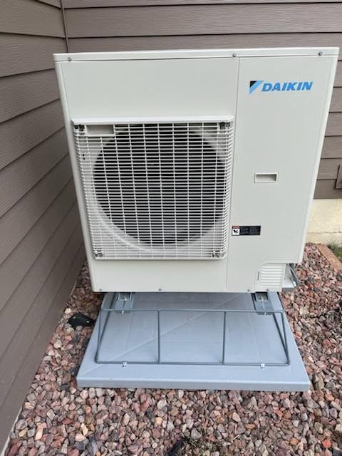 Daikin outdoor air conditioner unit on a gravel bed beside a house wall