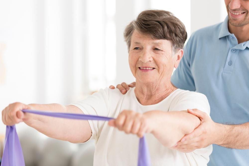 An Elderly Woman Is Doing Exercises With A Resistance Band — Port Macquarie Physio & Pilates In Port Macquarie, NSW