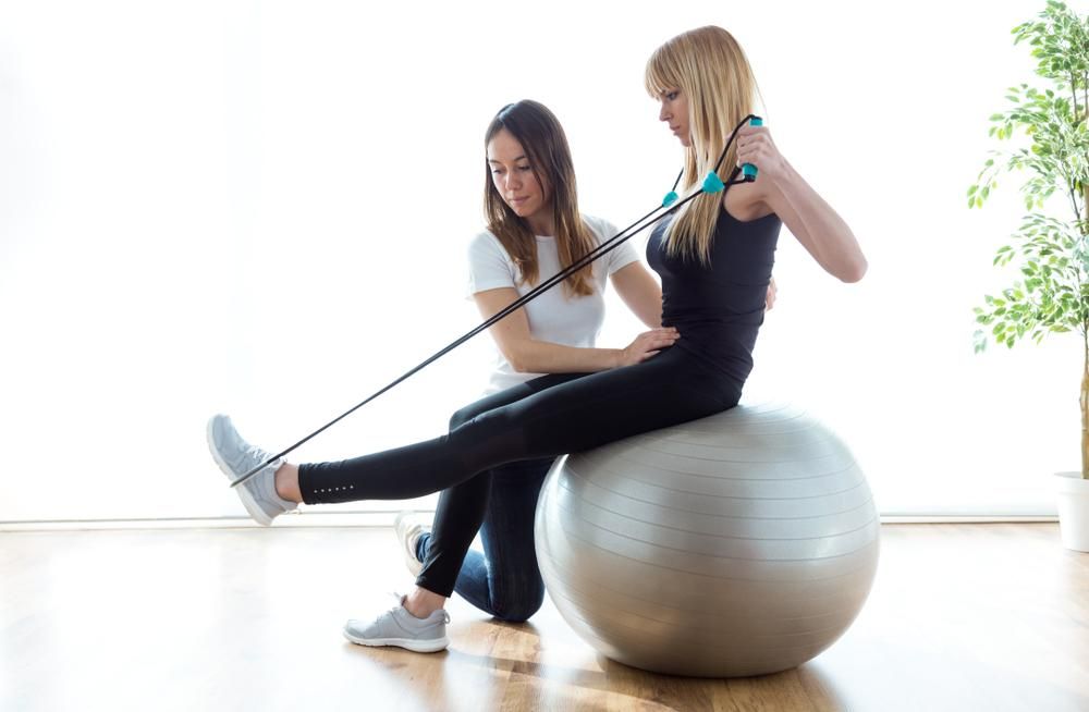 A Woman Is Sitting On An Exercise Ball With A Resistance Band — Port Macquarie Physio & Pilates In Port Macquarie, NSW