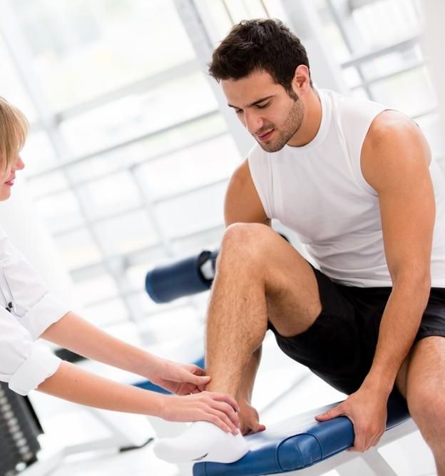 A Man Is Sitting On A Bench While A Woman Examines His Foot — Port Macquarie Physio & Pilates In Port Macquarie, NSW