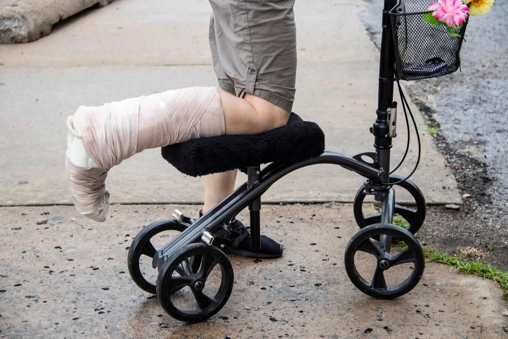 A Person With A Cast On Their Leg Is Sitting On A Knee Walker — Port Macquarie Physio & Pilates In Port Macquarie, NSW