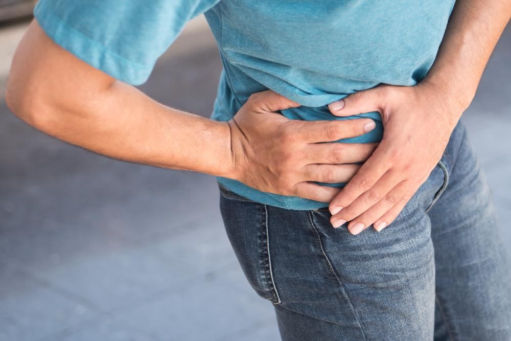 A Man Is Holding His Hip In Pain — Port Macquarie Physio & Pilates In Port Macquarie, NSW
