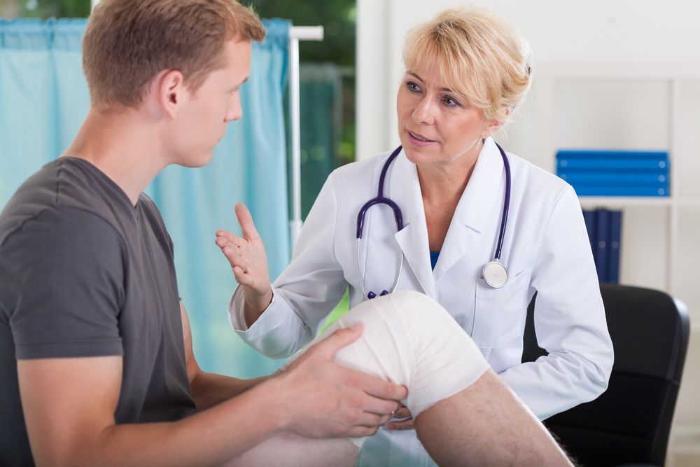 A Man With A Bandaged Knee Is Talking To A Doctor — Port Macquarie Physio & Pilates In Port Macquarie, NSW