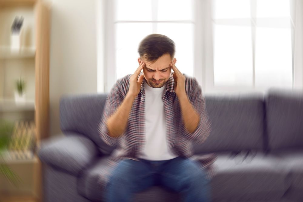 A man is sitting on a couch with his hands on his head. — Port Macquarie Physio & Pilates In Port Macquarie, NSW