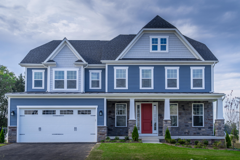 Two-story gray house with white trim, red front door, and attached garage under a cloudy sky