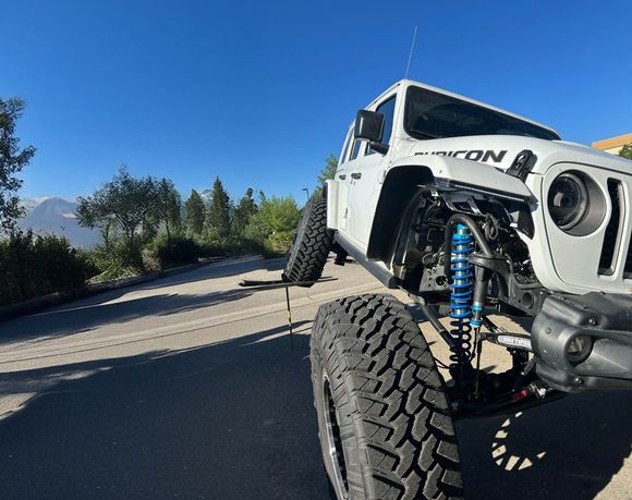 White off-road truck with large tires on a mountain road under a clear blue sky