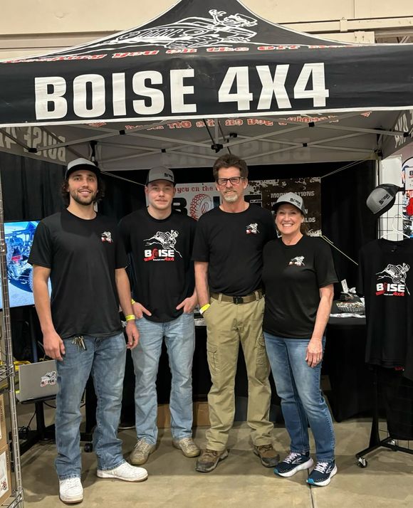 Four people pose under a Boise 4x4 tent at an outdoor event, wearing black shirts.