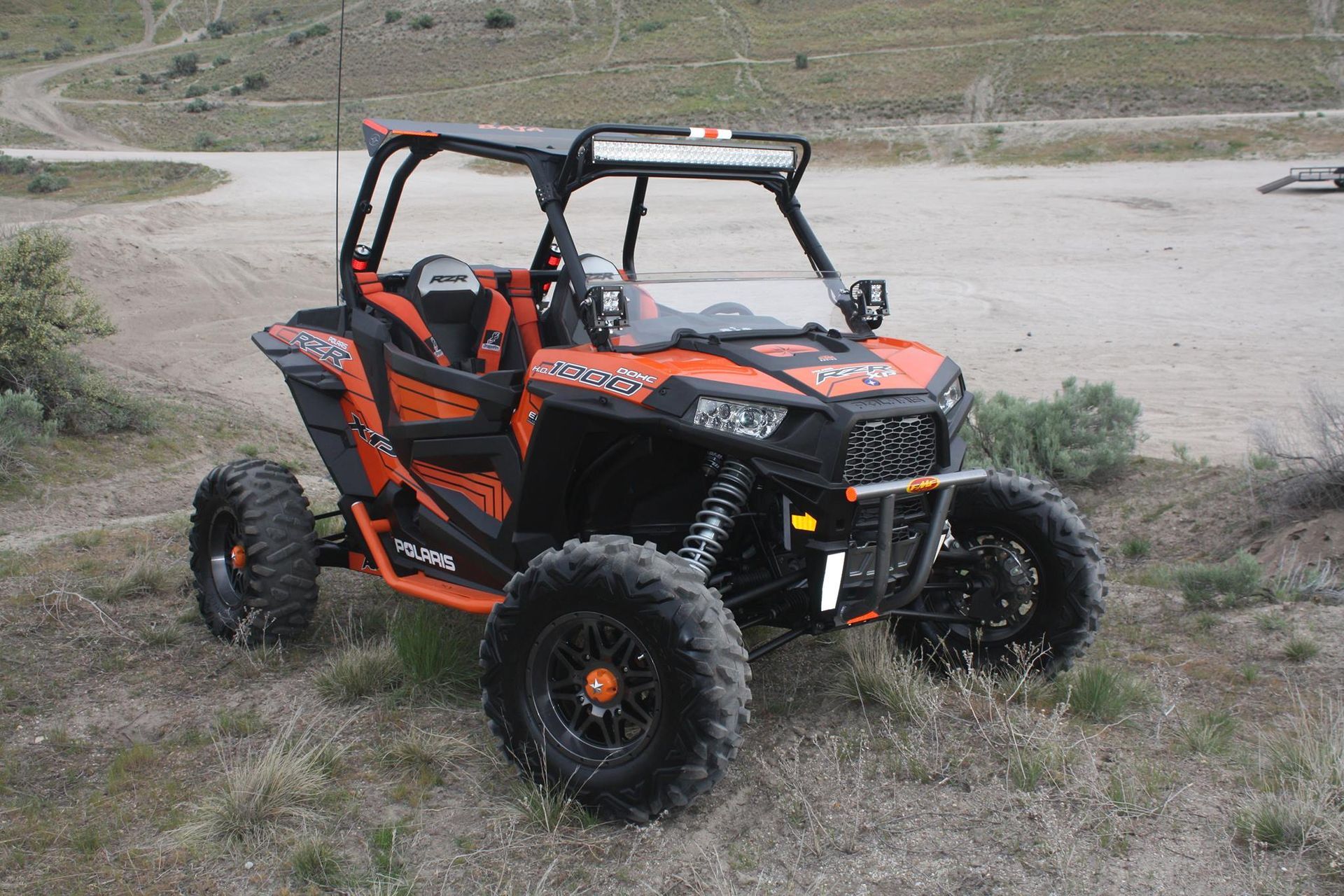Orange and black Polaris RZR off-road vehicle parked on a dirt trail.