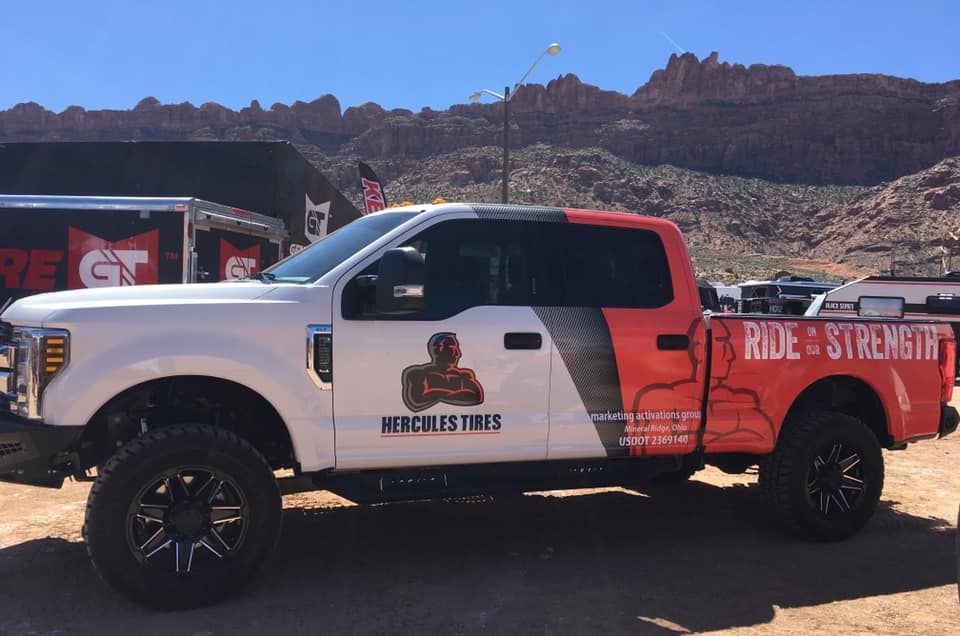 A white, black, and orange Hercules Tires pickup truck with 