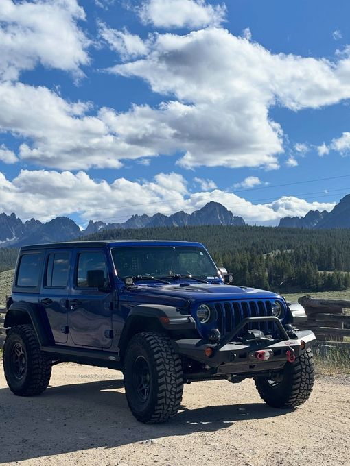 A dark blue Jeep Wrangler parked on a dirt path with rugged, jagged mountains — 4 x 4 shops near me